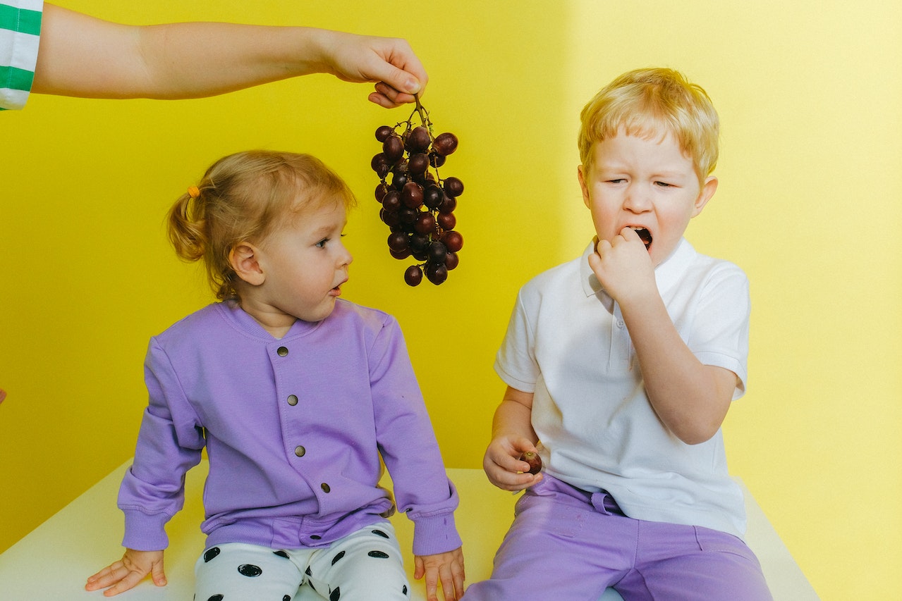 Na zdjęciu widać dzieci, które z apetytem jedzą słodkie winogrona. Ich uśmiechnięte twarze i zadowolenie z jedzenia owoców doskonale oddają radość, jaką przynosi im jedzenie zdrowych i smacznych produktów. Winogrona, pełne witamin i minerałów, stanowią doskonałą przekąskę dla najmłodszych, a ich słodki smak z pewnością przypadnie do gustu każdemu dziecku
